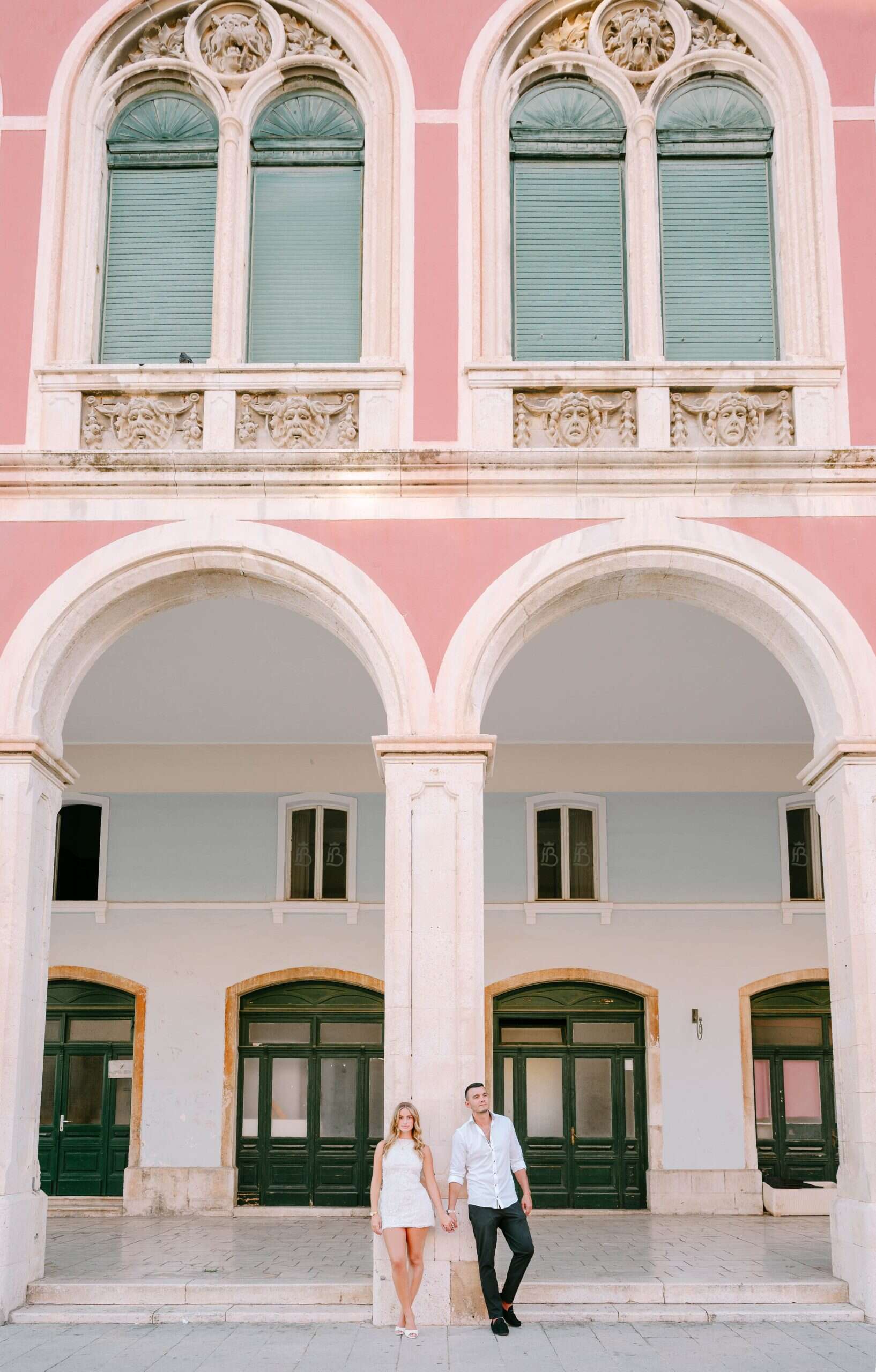 Ružičasta povijesna zgrada s lučnim prozorima i parom koji stoji ispred.