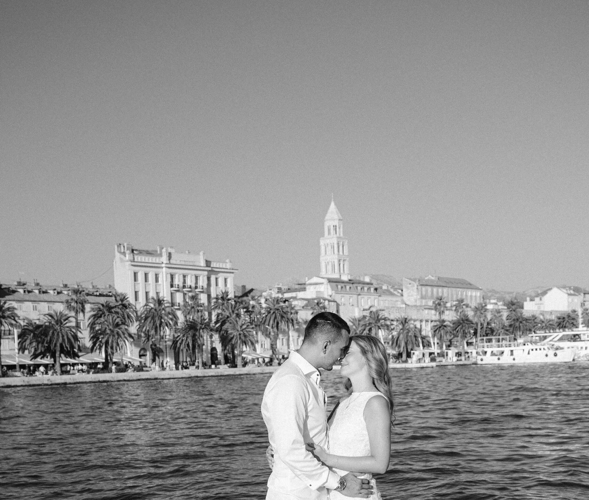 Crno-bijela filmska fotografija para uz more, vizura grada Splita u daljini.