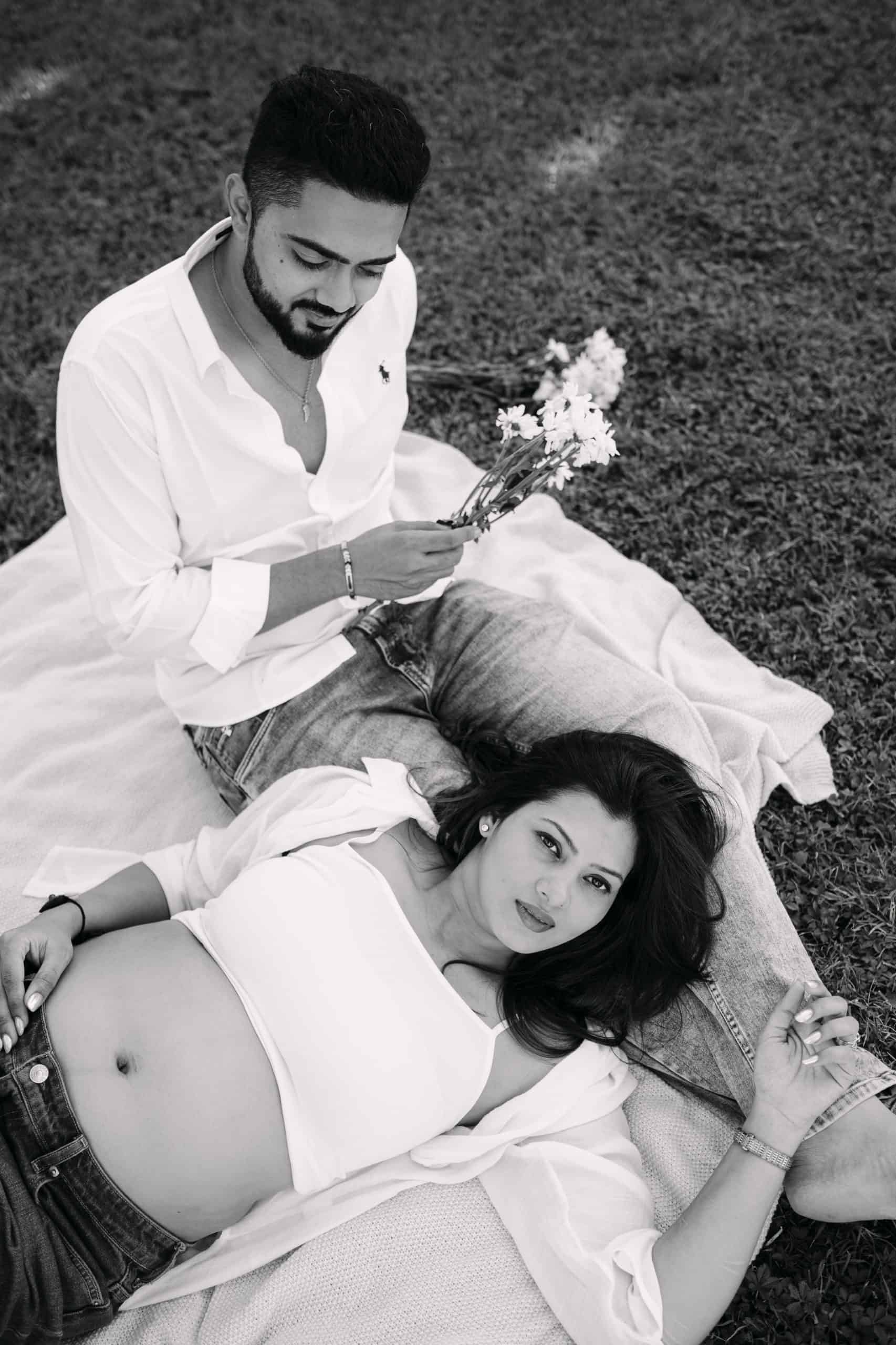 Buduća majka i suprug na travnjaku s cvijećem, romantična fotografija.