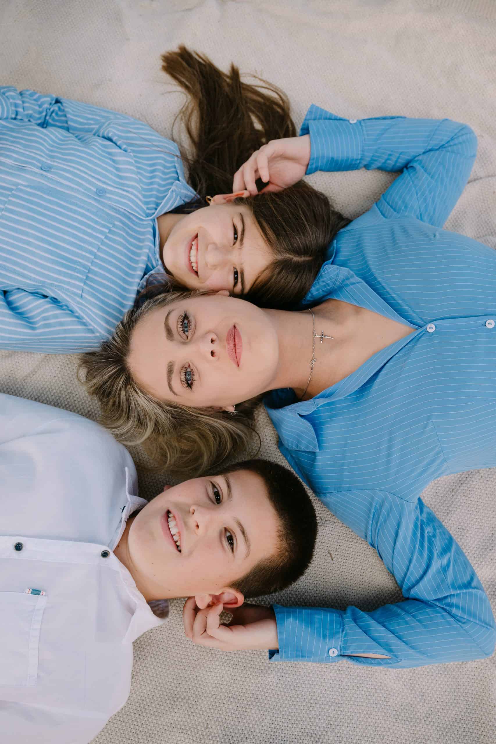 Sretni mladi odrasli leže na bež dekici, smiješe se i gledaju u kameru, odjeveni u ležerno plavu odjeću.