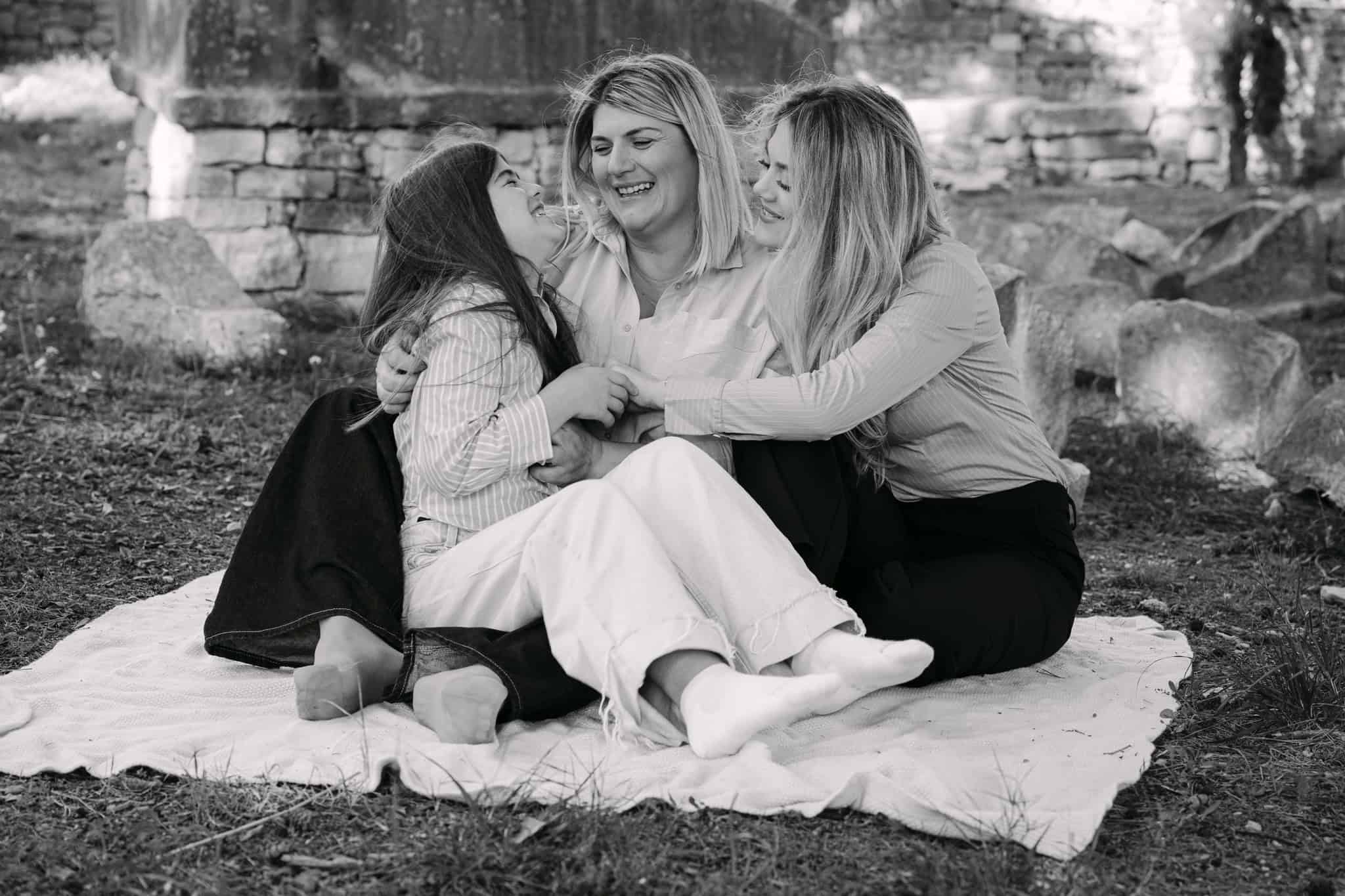 Majka i kćerke sjede na deki vani, smiješe se i grle se.