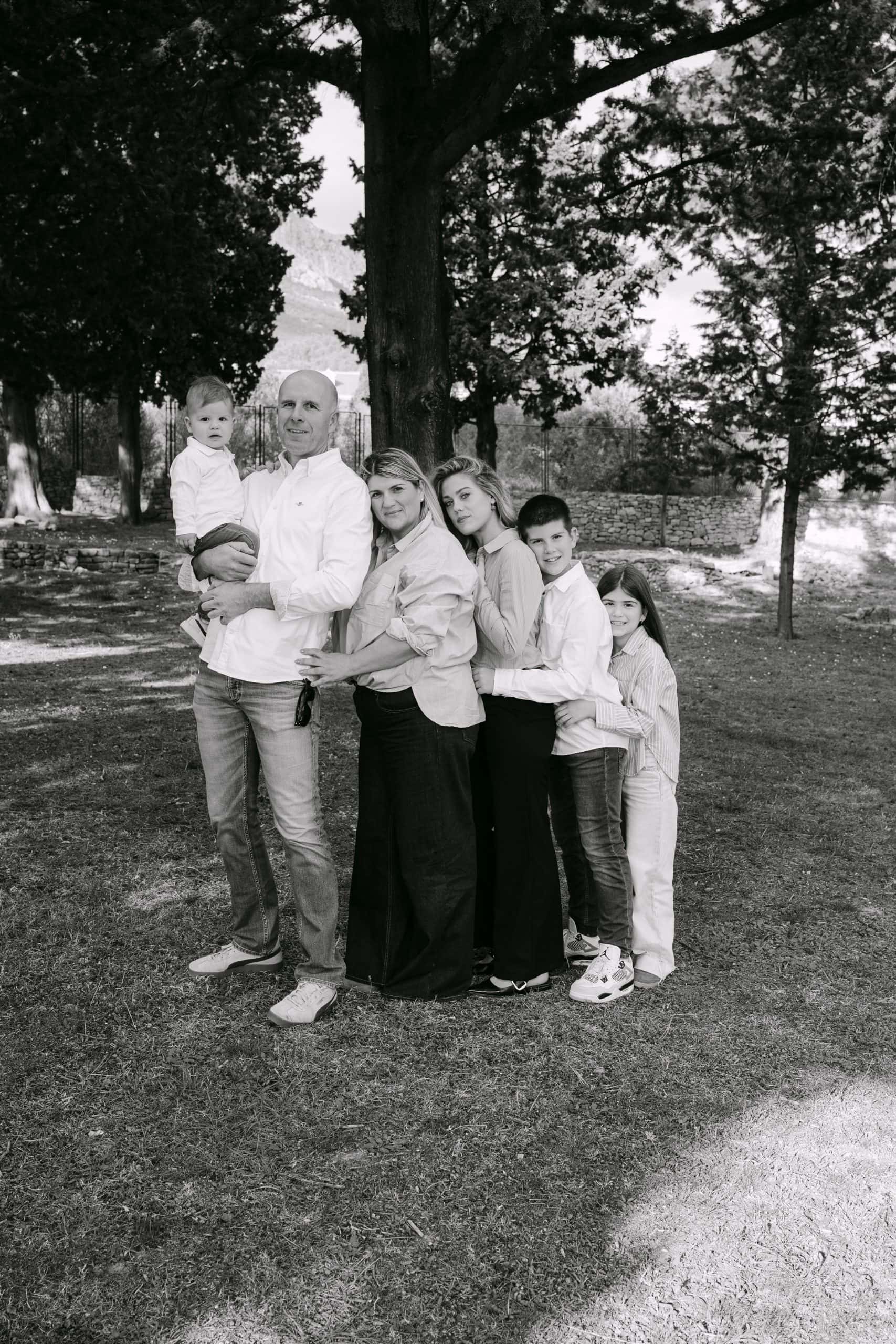 Obiteljski portret na otvorenom u crno-bijeloj tehnici, koji bilježi radostan trenutak pod velikim drvetom.