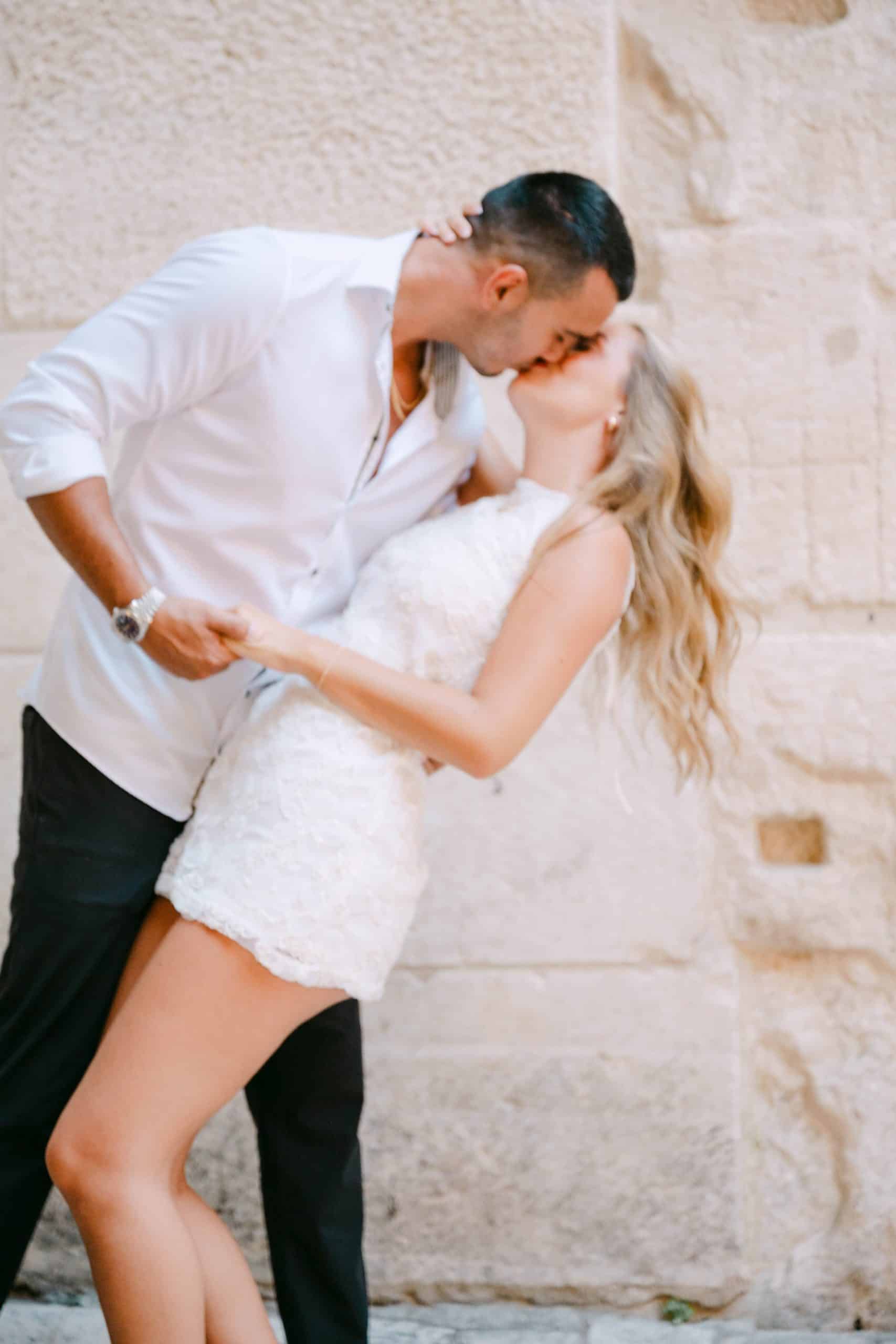 Par dijeli poljubac tijekom fotografiranja uz rustikalni kameni zid u gradu Splitu.