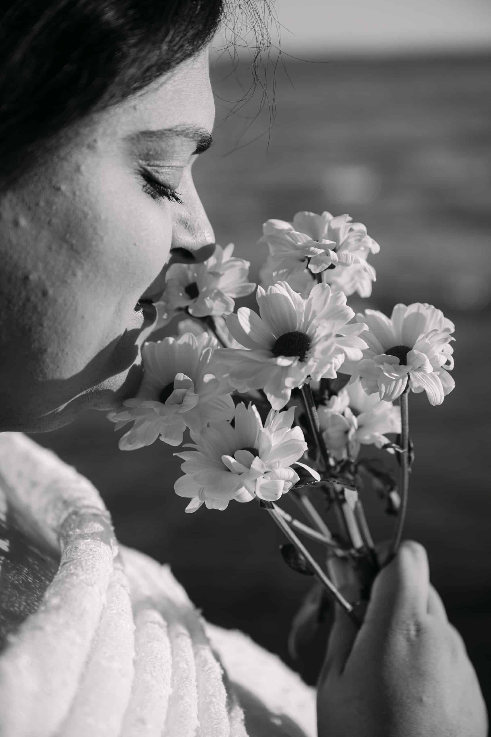 Žena miriše cvijeće vani blizu mora, crno-bijela fotografija.