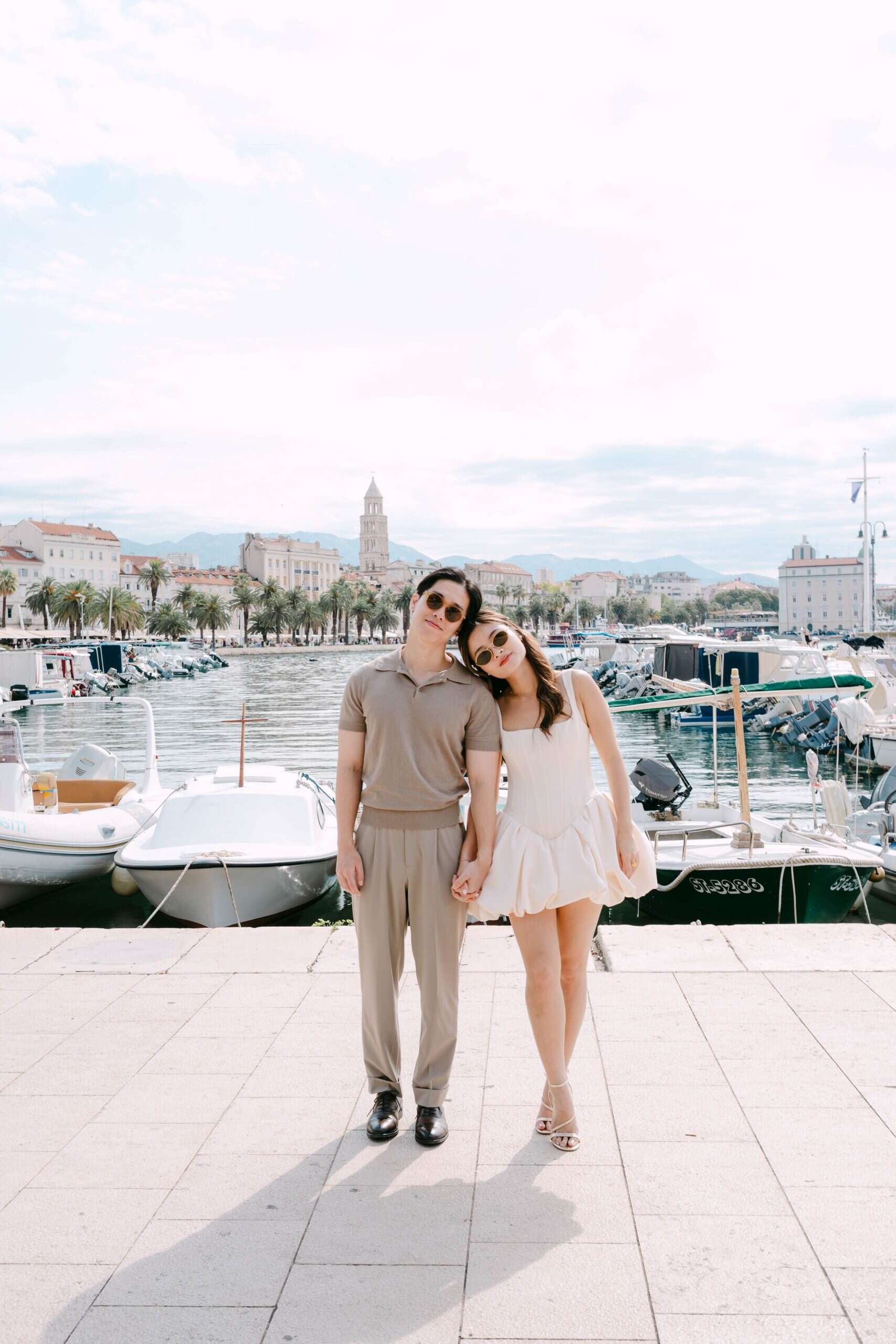 Portret para u splitskoj marini s brodovima i gradskom panoramom u pozadini.