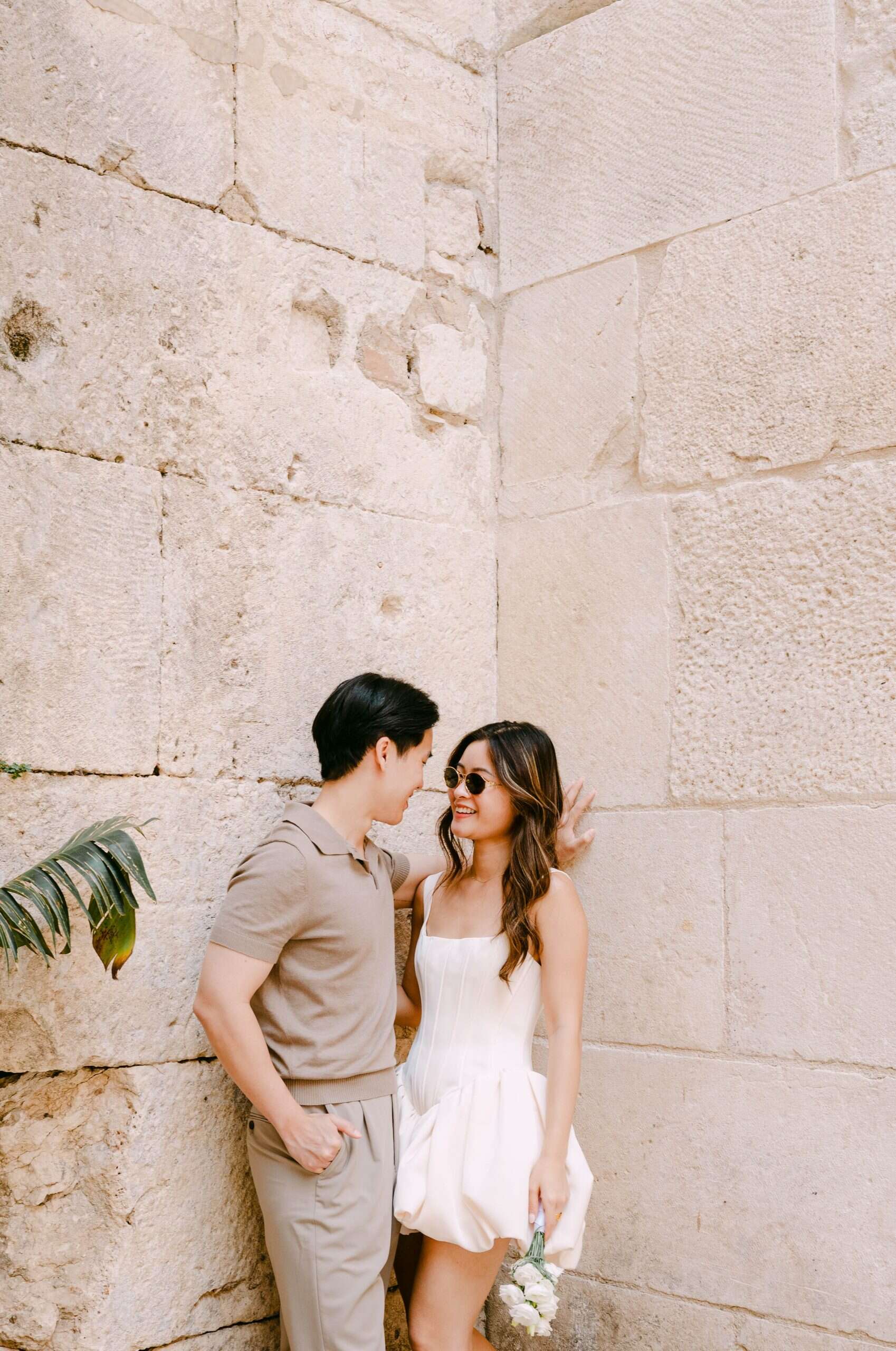 Romantični par stoji blizu teksturiranog kamenog zida, hvatajući ljubav i povezanost u trenutku.