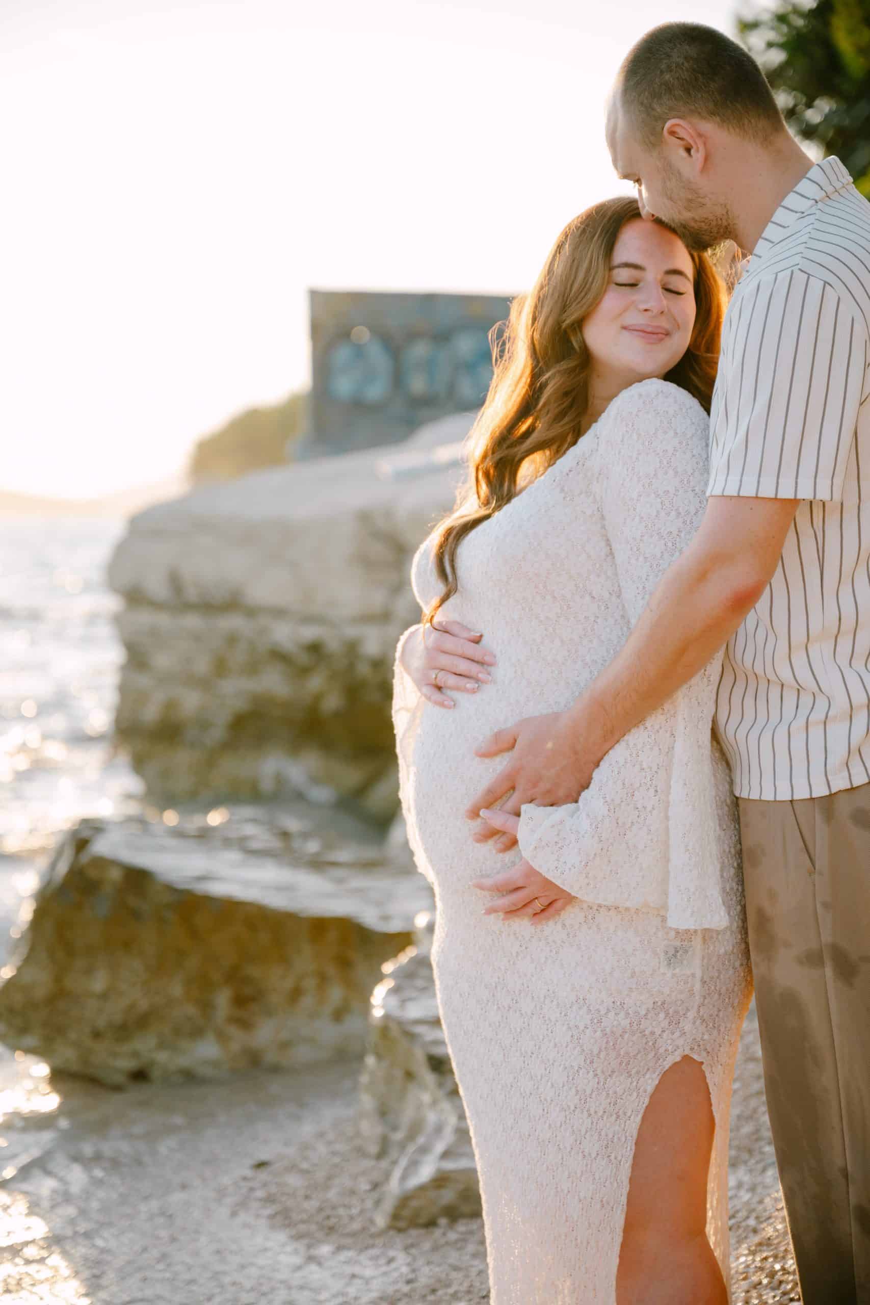 Trudnica i partner se grle na plaži u zalazak sunca.