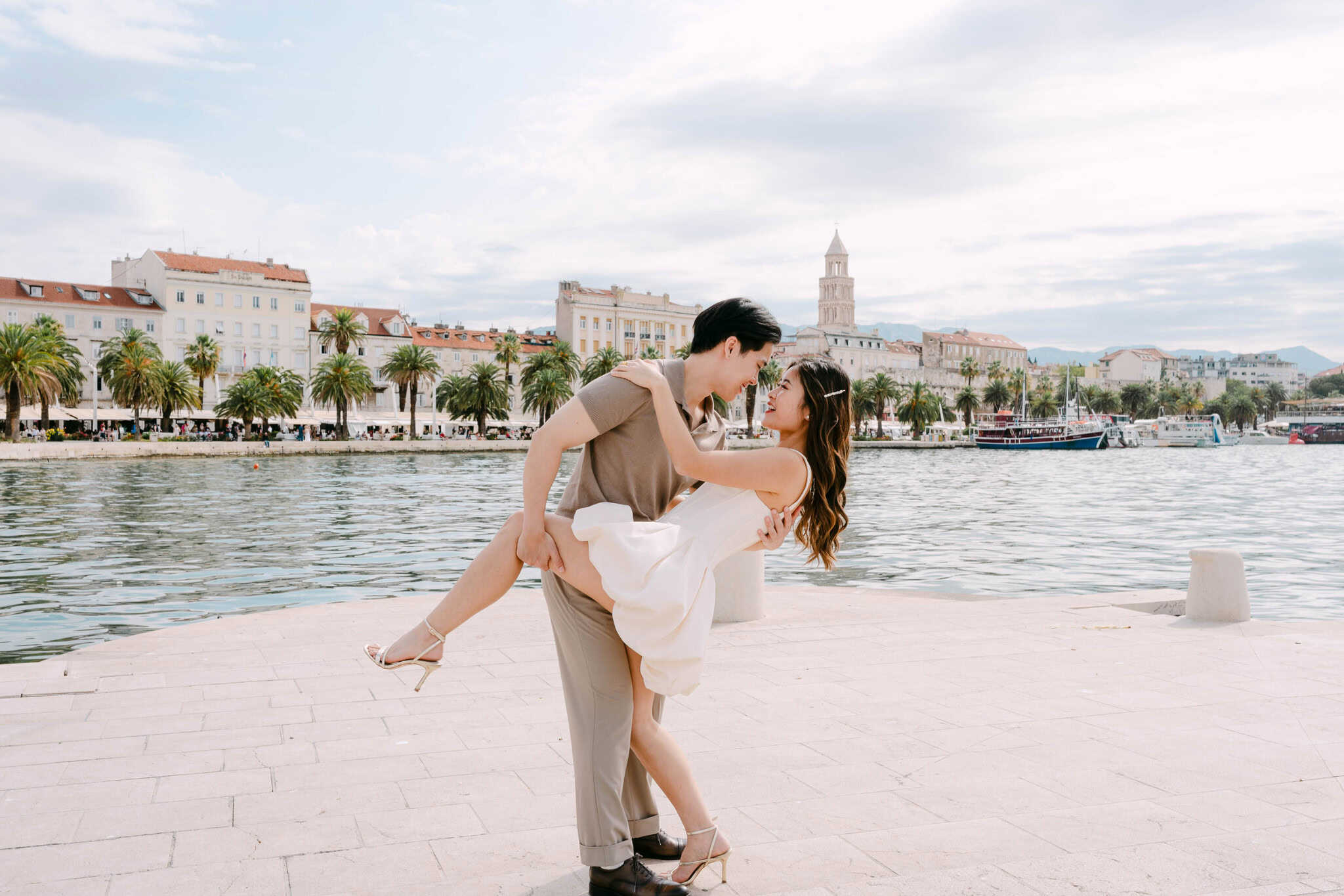 Portret para koji se gleda i smije u blizini luke grada Splita s povijesnim zgradama u pozadini.