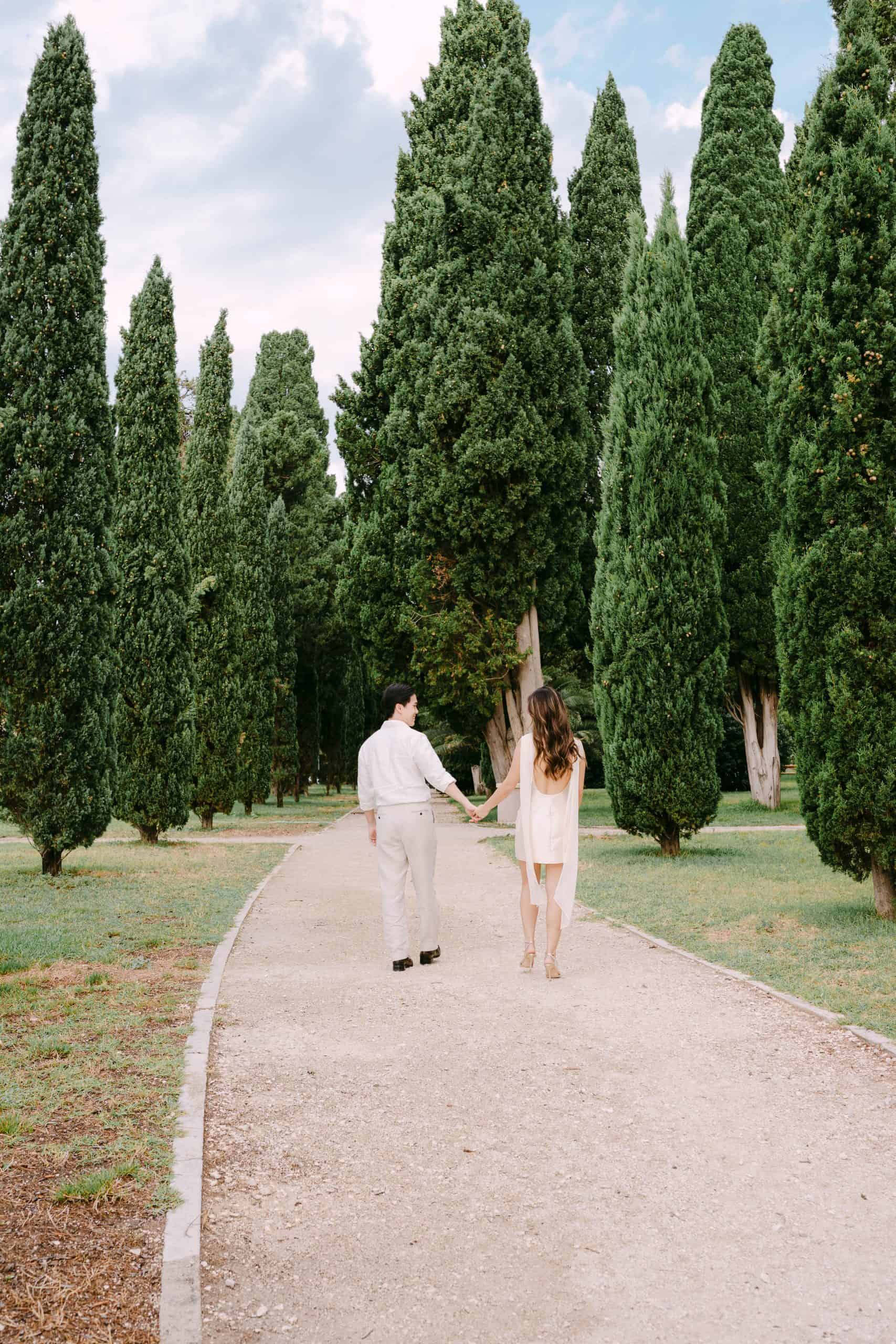 Par šeta ruku pod ruku kroz bujne čemprese u mirnom okruženju parka Sustipana u Splitu.
