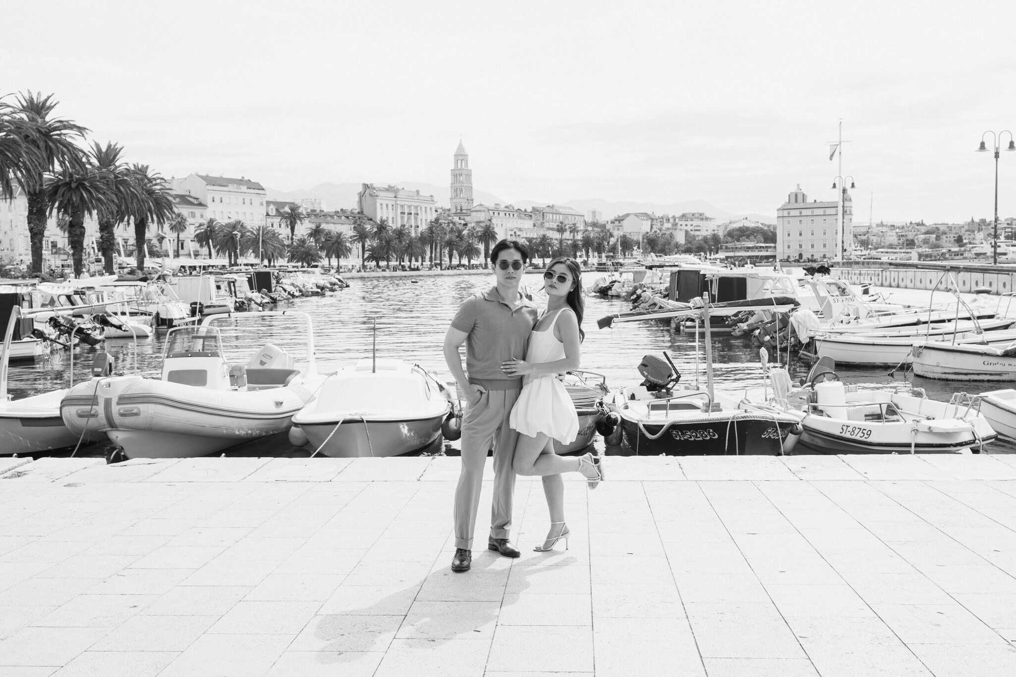 Prekrasan par stoji uz luku u Hrvatskoj, s brodovima i povijesnim gradskim pejzažom u pozadini.