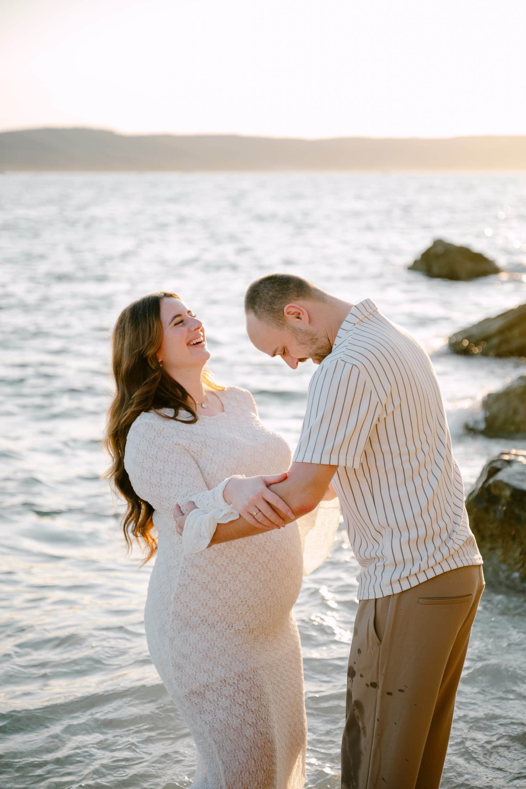 Romantična fotografija trudnice i partnera na obali mora.