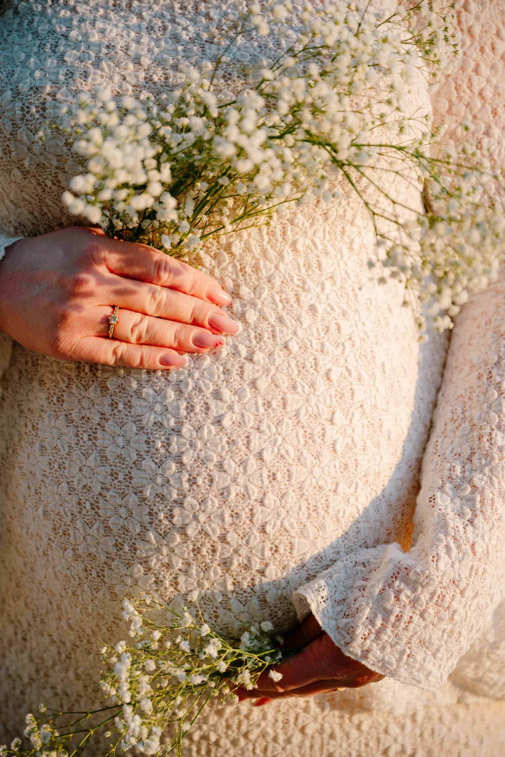 Buduća majka s buketom cvijeća i detaljima odjeće.