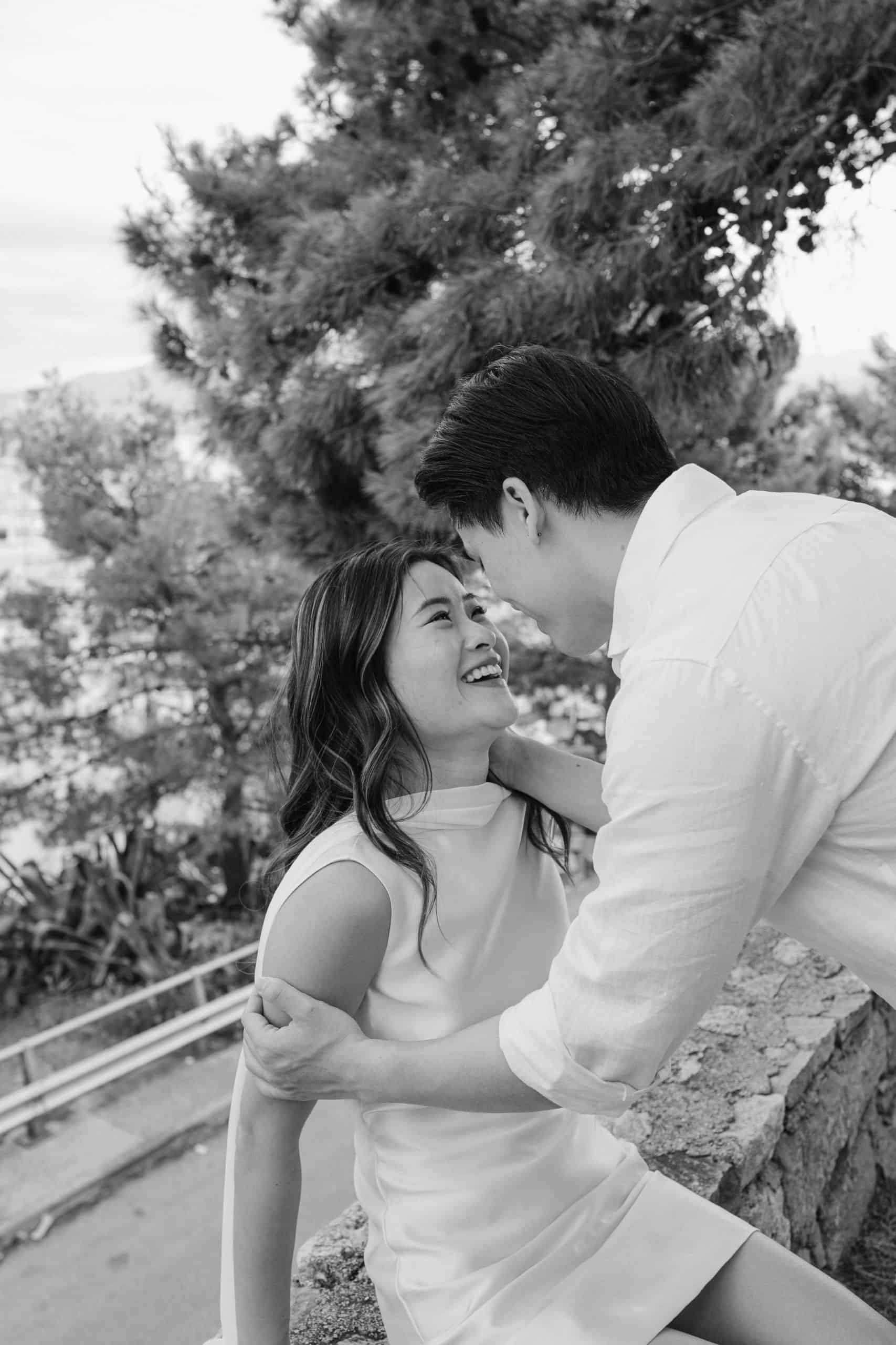 Romantični par se grli na otvorenom, smiješi se, s drvećem u pozadini.