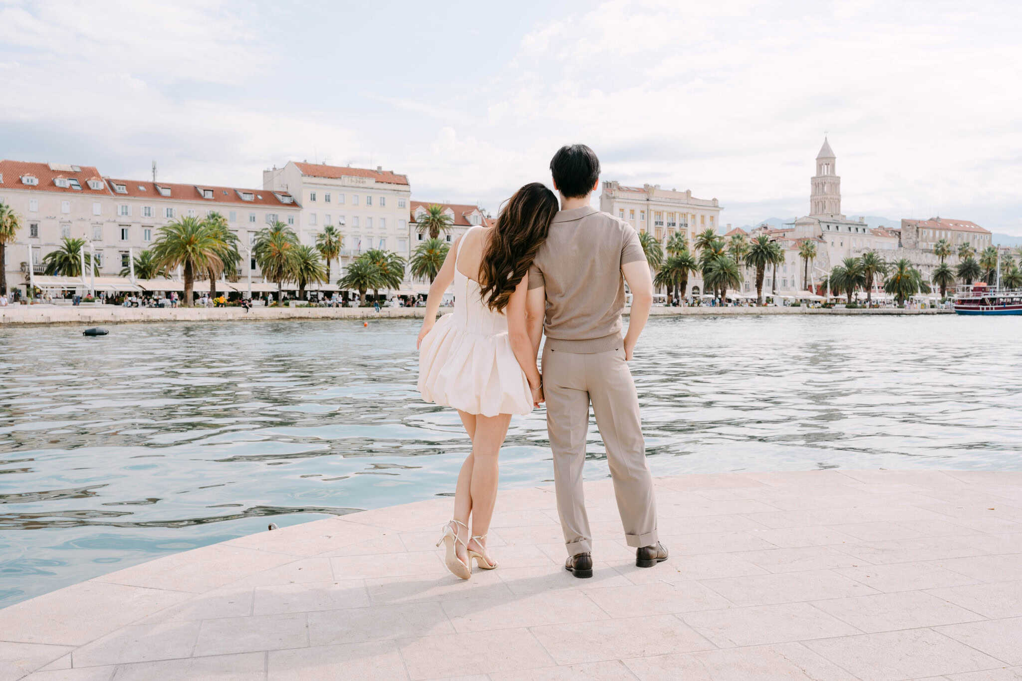 Par stoji uz more s gradskim pejzažom i povijesnim zgradama u pozadini.