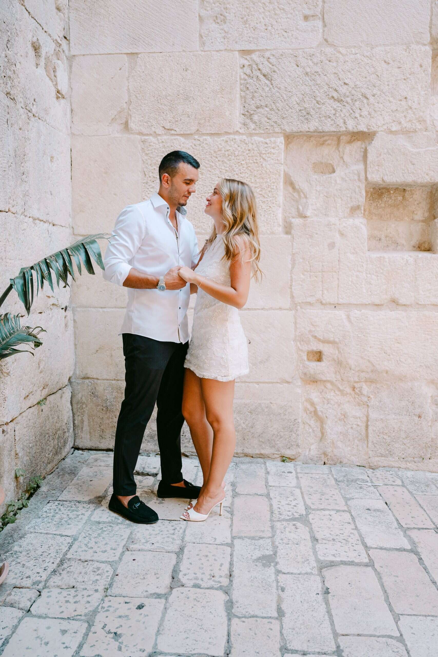 Par se drži za ruke uz drevni kameni zid na otvorenom.