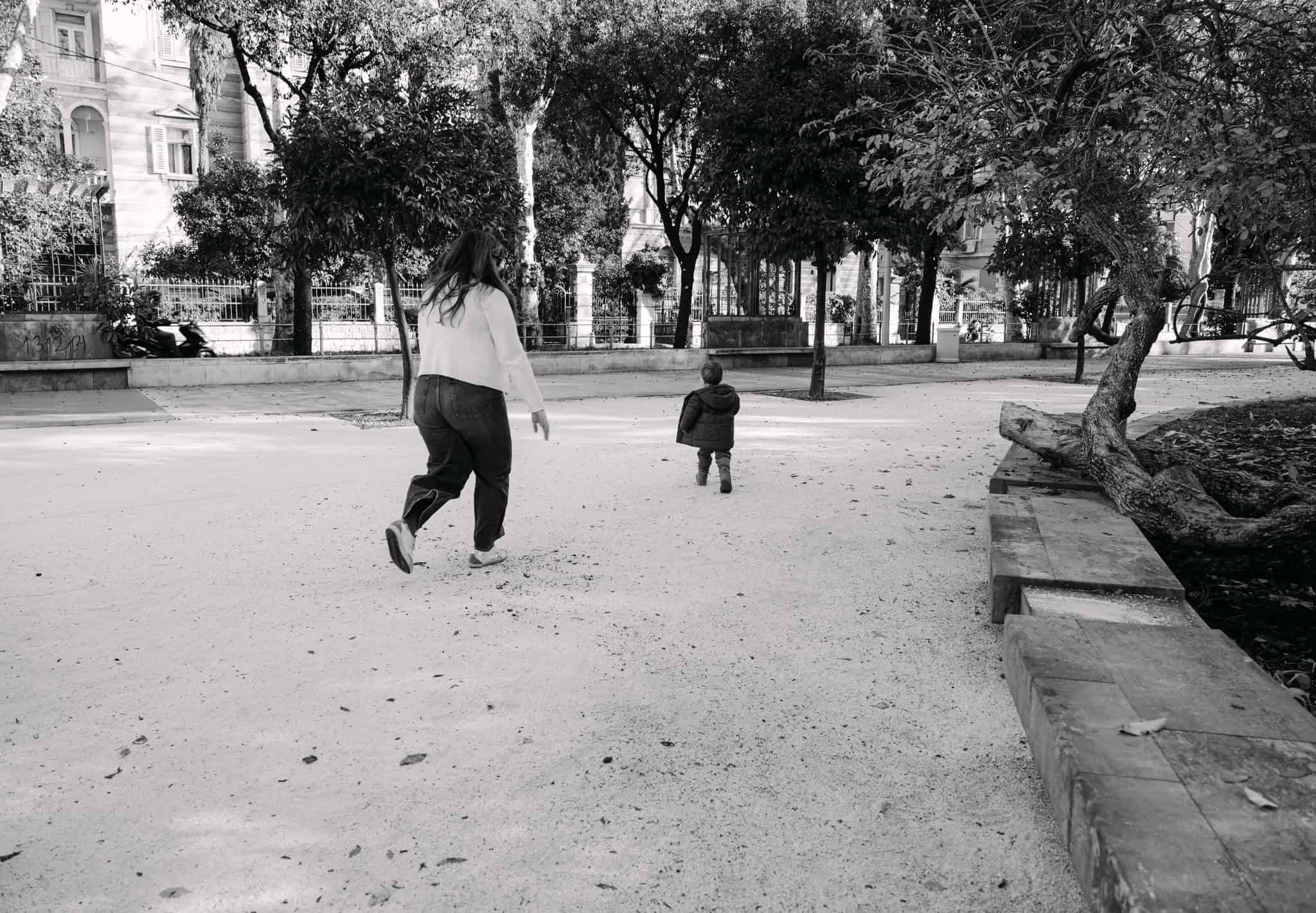 Gradski park sa ženom i djetetom dok trče, crno-bijela fotografija.