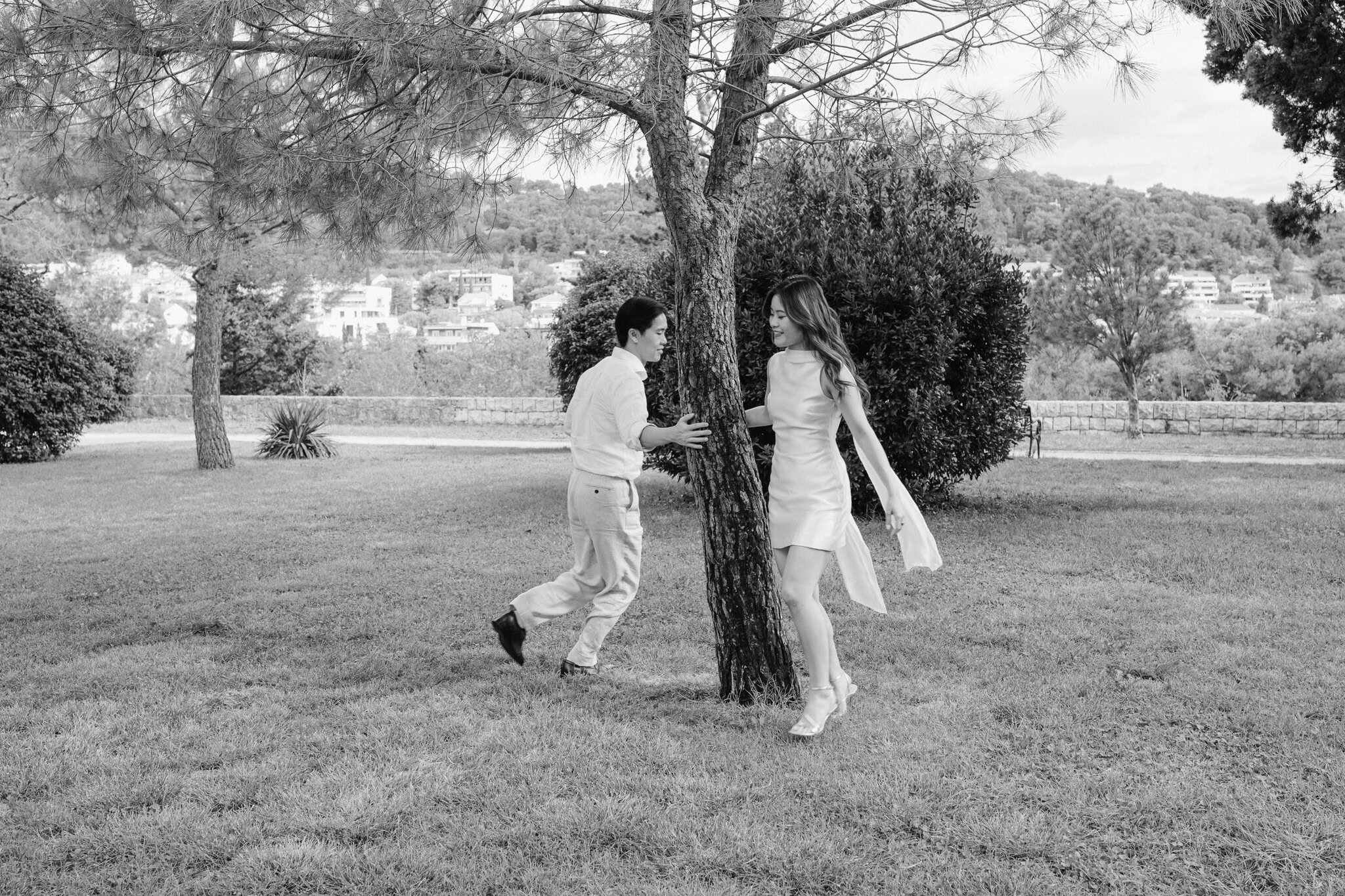 Muž i žena se igraju oko drveta u parku, bilježeći radosne trenutke na otvorenom.