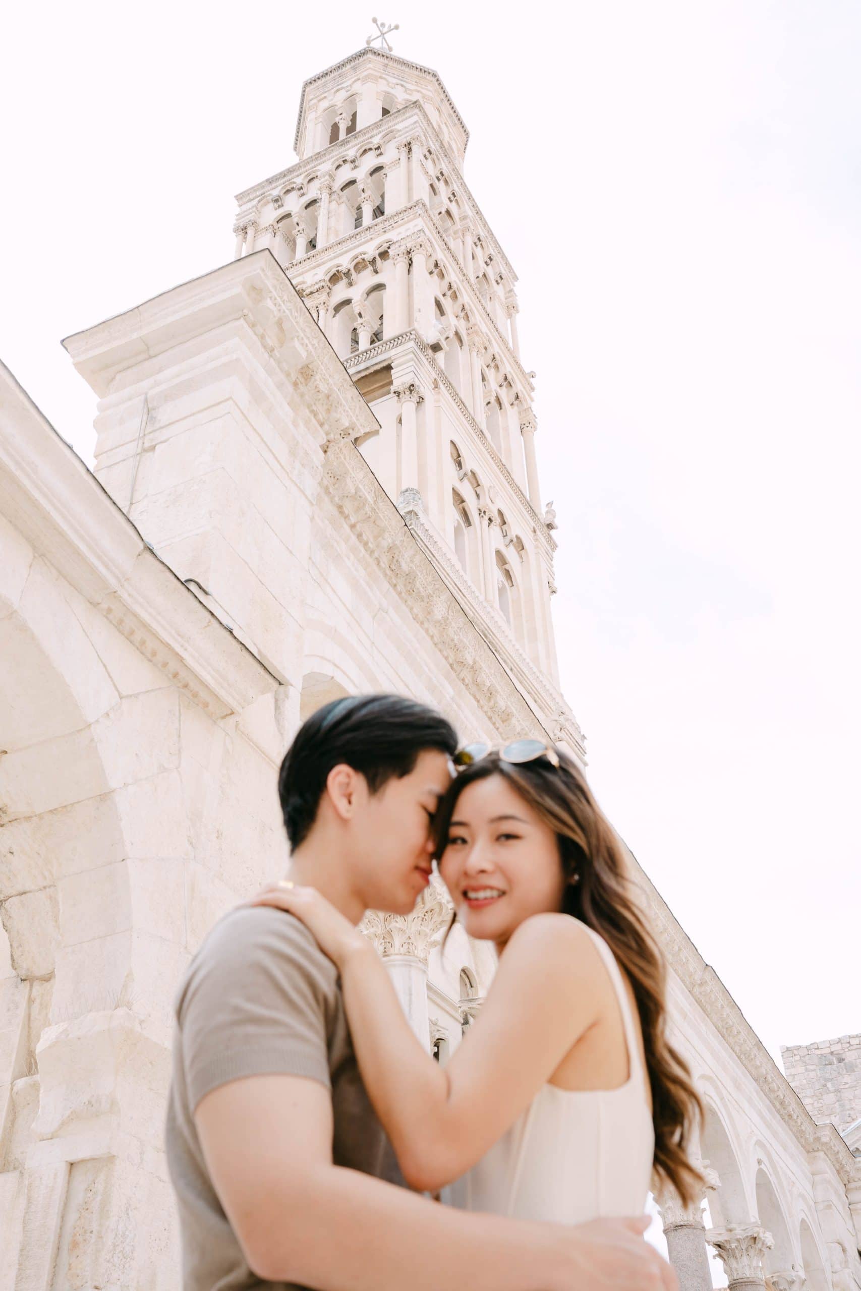 Romantični par se grli ispred povijesnog zvonika Sv. Duje u Splitu, bilježeći ljubav i arhitekturu.