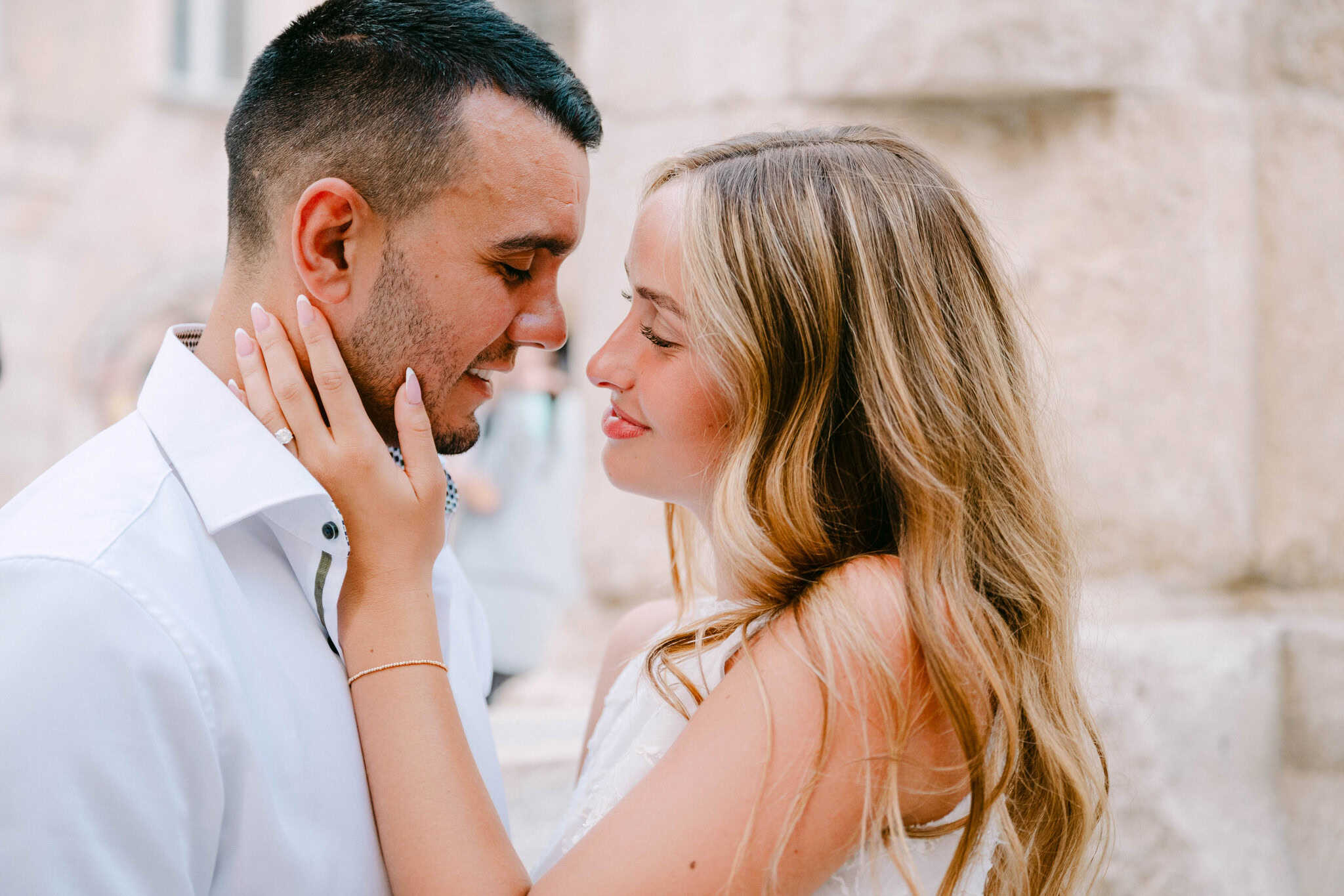 Budući mladenci stoje jedno nasuprot drugome dok žena dlanovima dodiruje muškarčevo lice.