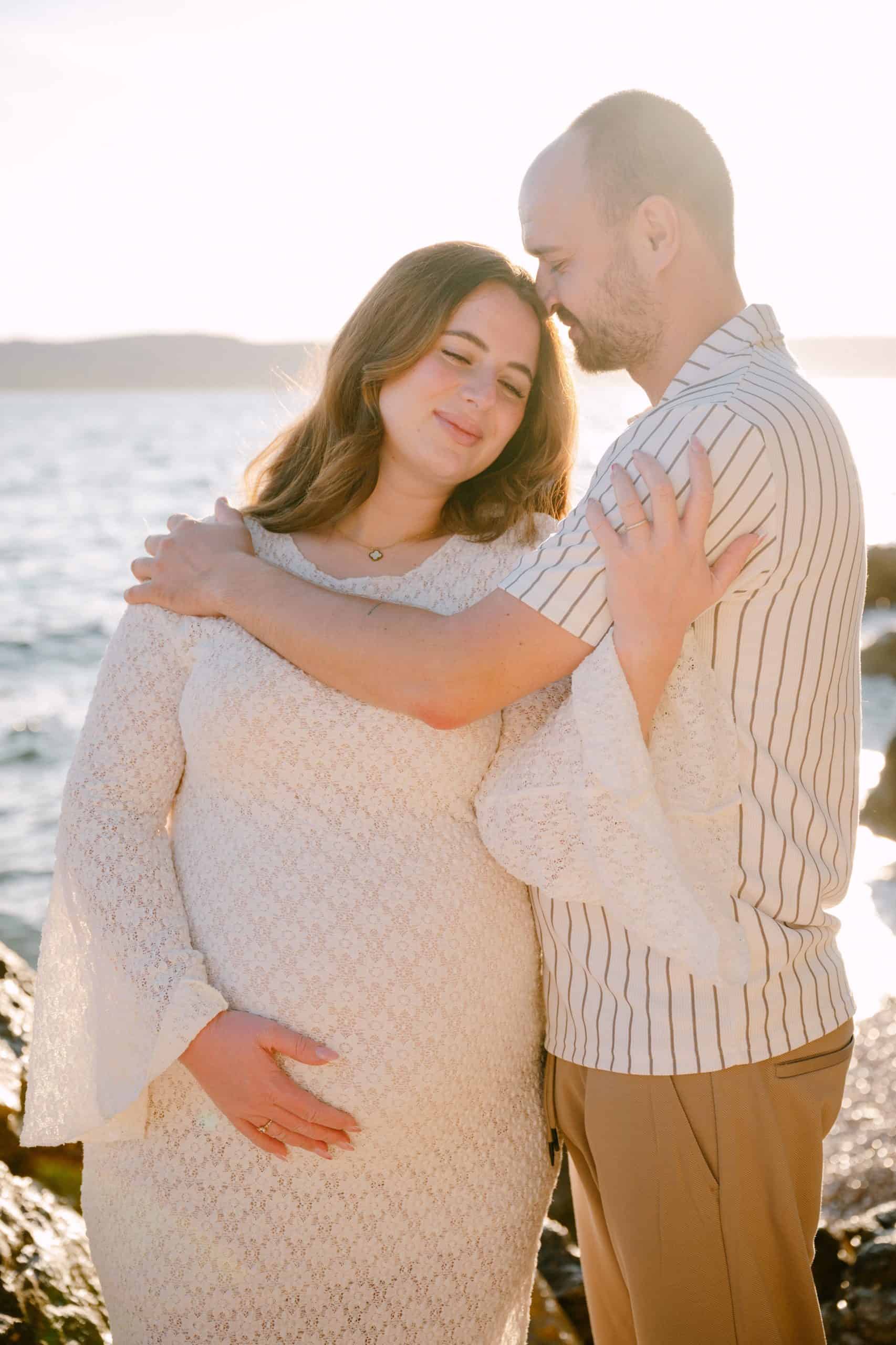 Nježan zagrljaj trudnice i supruga na stijenama uvale Obojena u Splitu tijekom zlatnog sata.