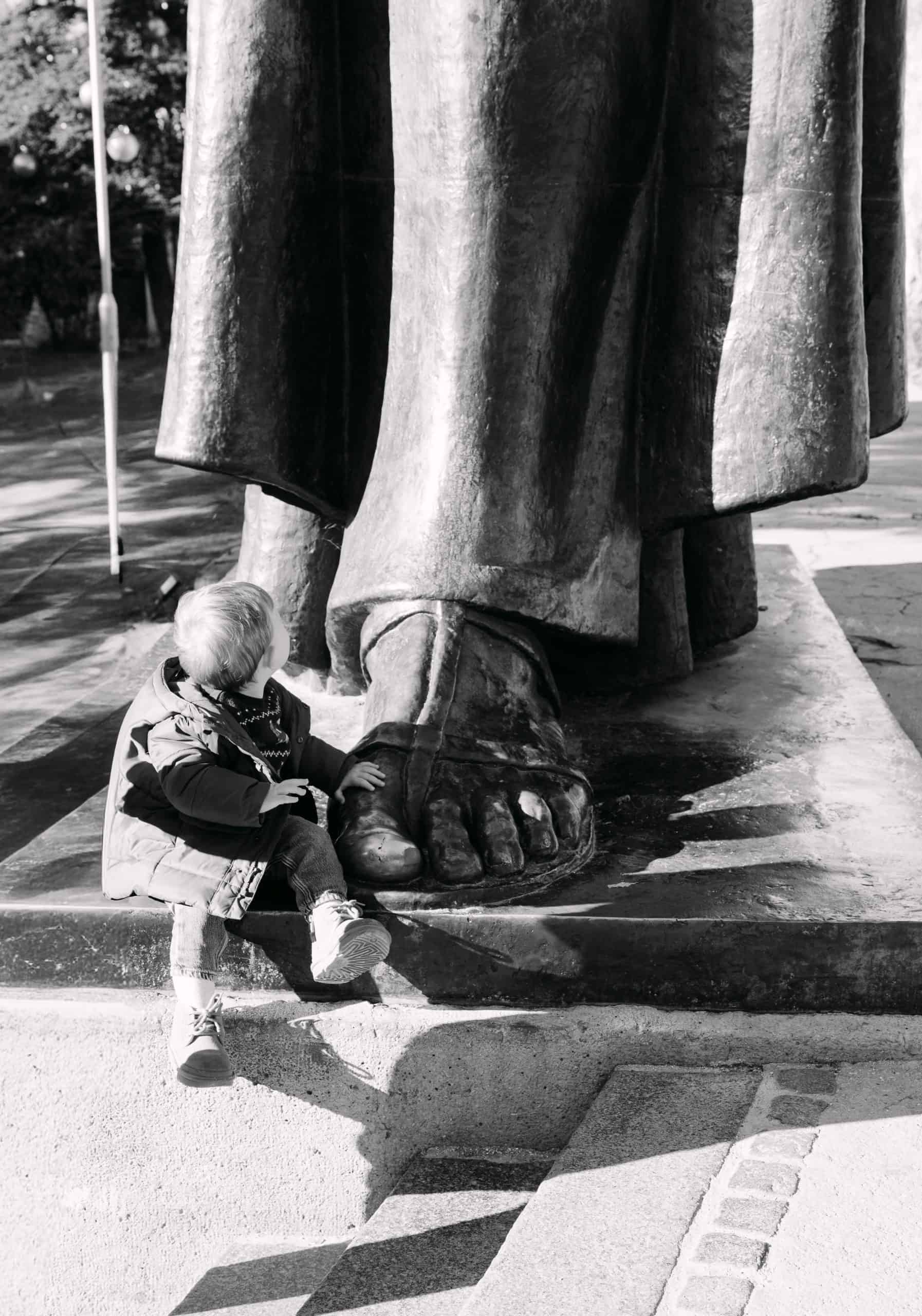 Kip povijesne osobe s djetetom koje sjedi u podnožju, bilježi trenutak znatiželje.