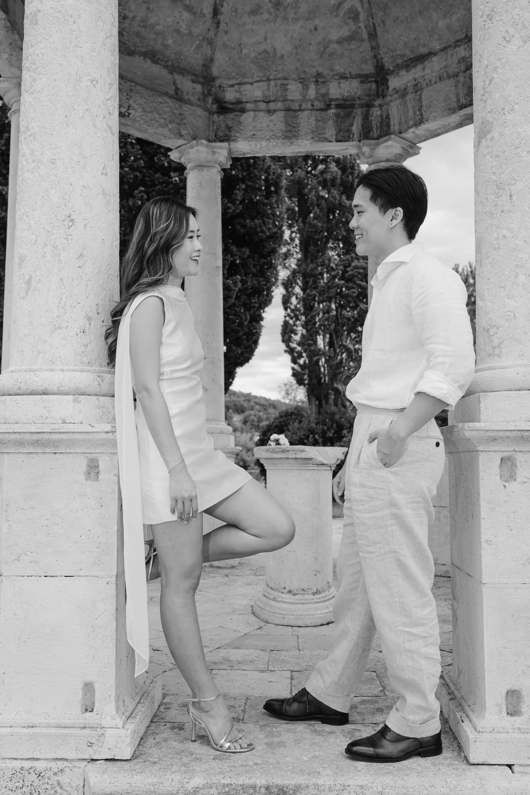 Elegantni portret para u klasičnom arhitektonskom okruženju parka Sustipana sa stupovima i zelenilom.