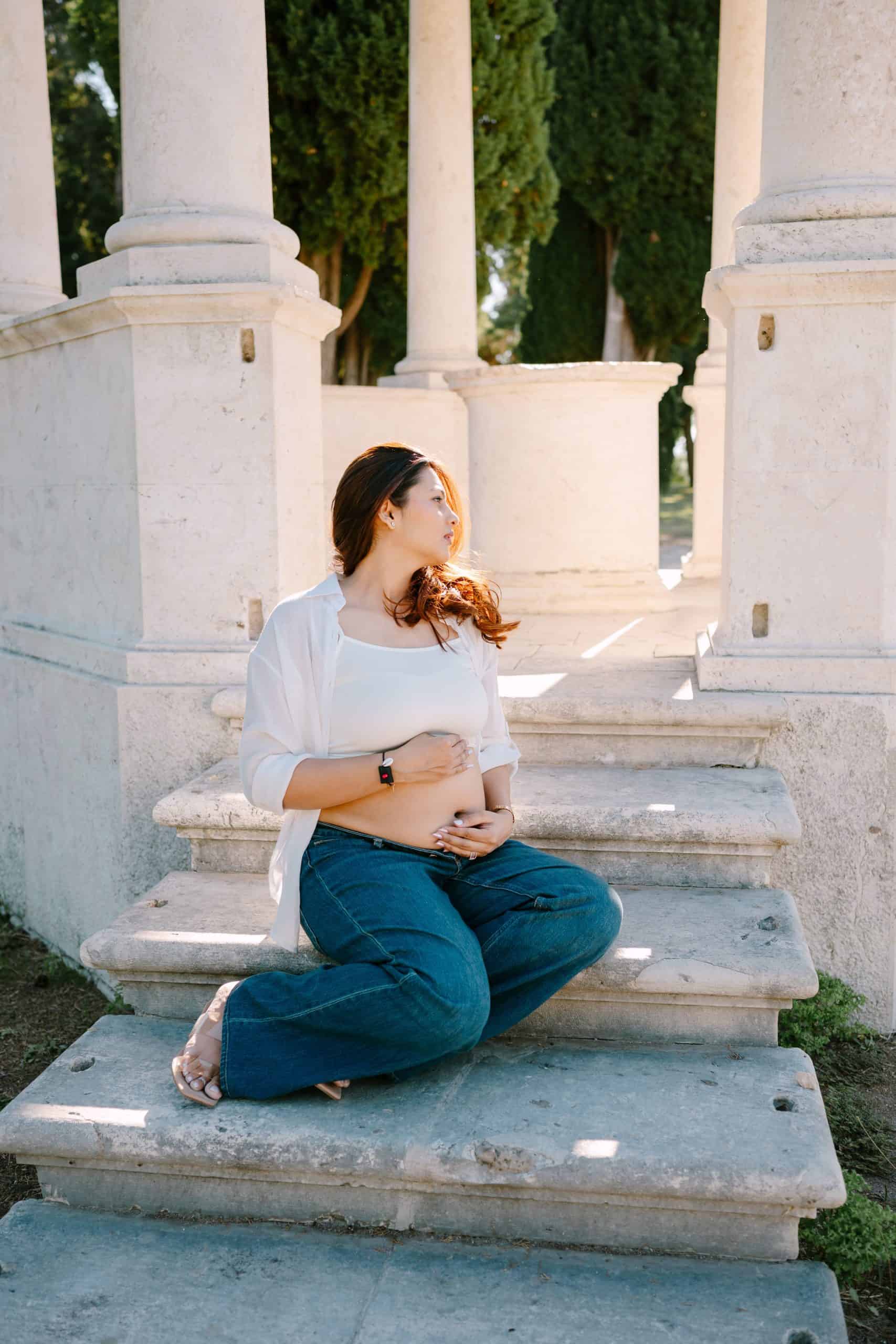 buduća majka sjedi na stepenicama u prirodnom okruženju, uživajući u mirnom trenutku.
