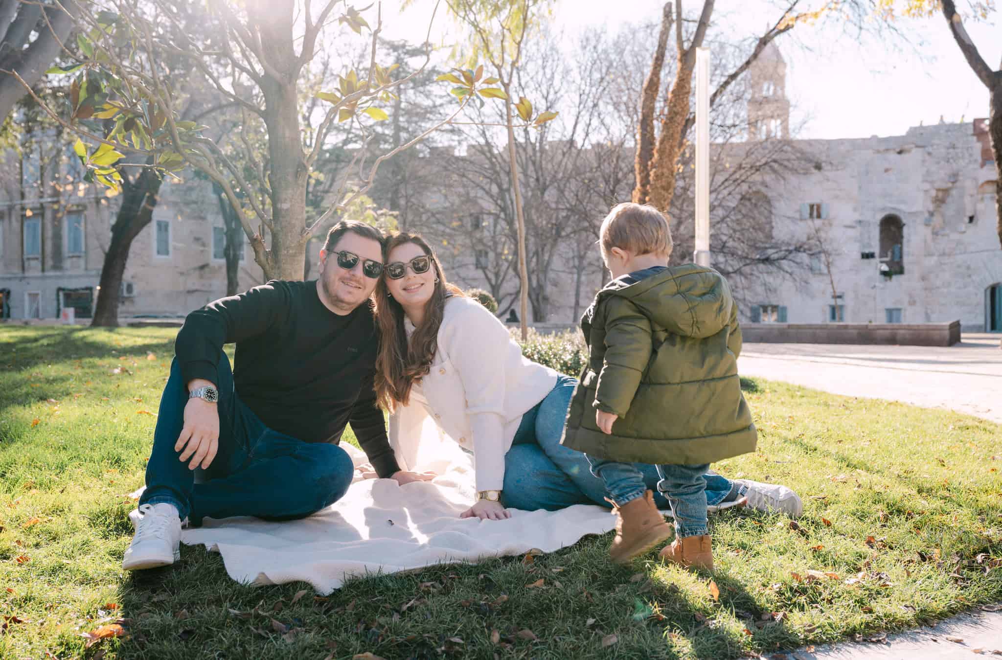 Obitelj uživa u sunčanom danu u parku s povijesnim ruševinama u pozadini.