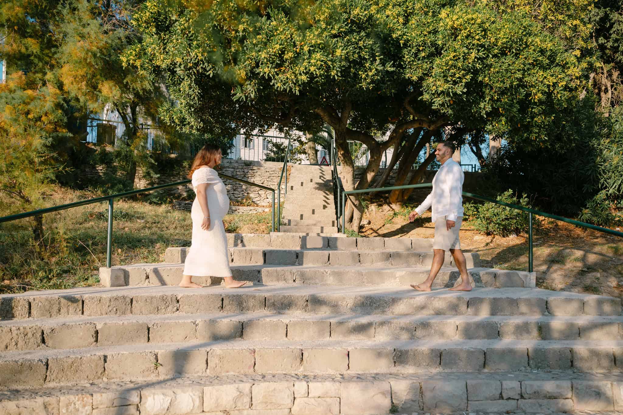 Dvoje ljudi hodaju jedan prema drugome na kamenim stepenicama s drvećem u pozadini.