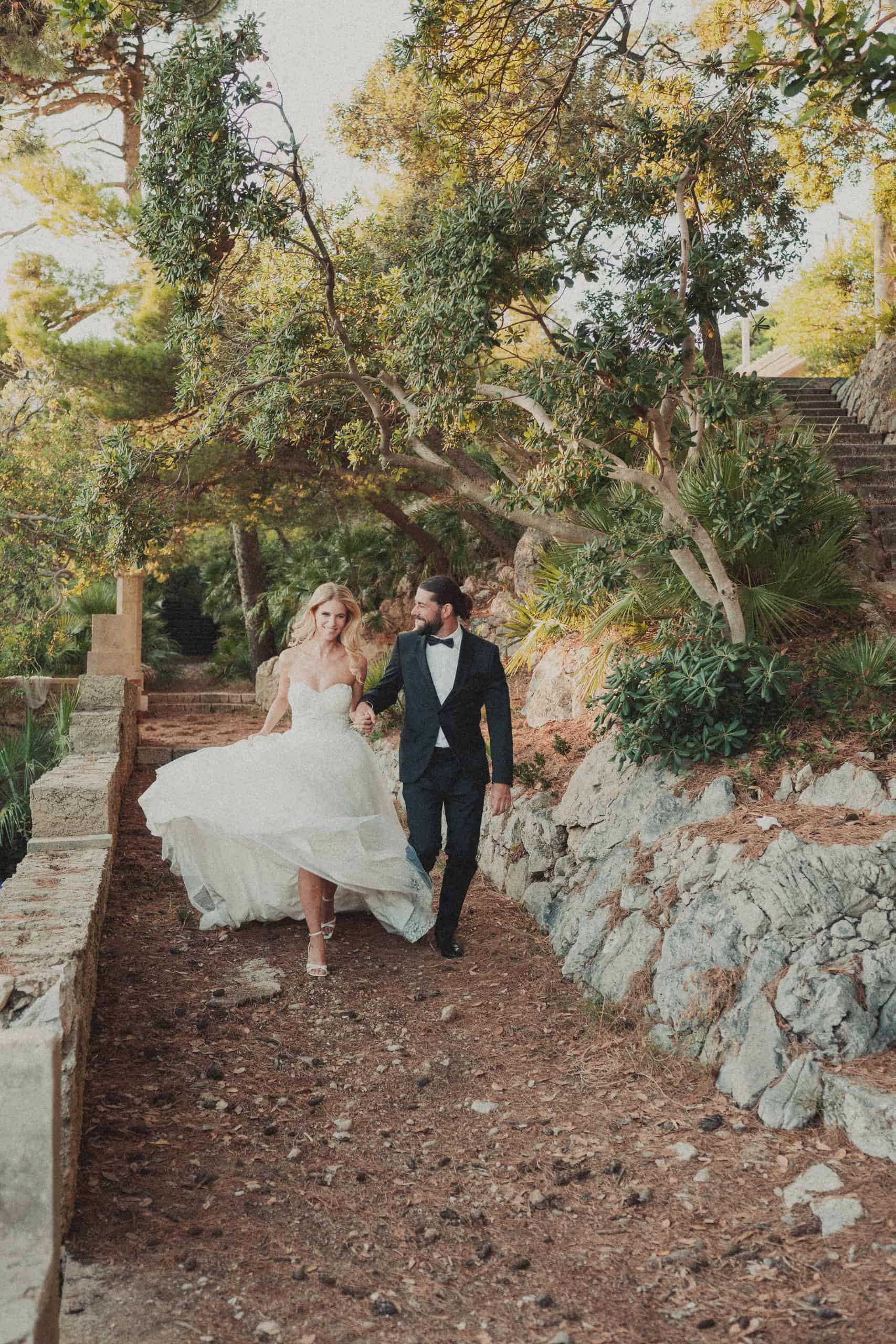 Nasmiješeni mladenci se drže za ruke i ležerno trče mediteranskom stazom okruženi borovima i povijesnim kamenim zidovima u Dubrovniku.