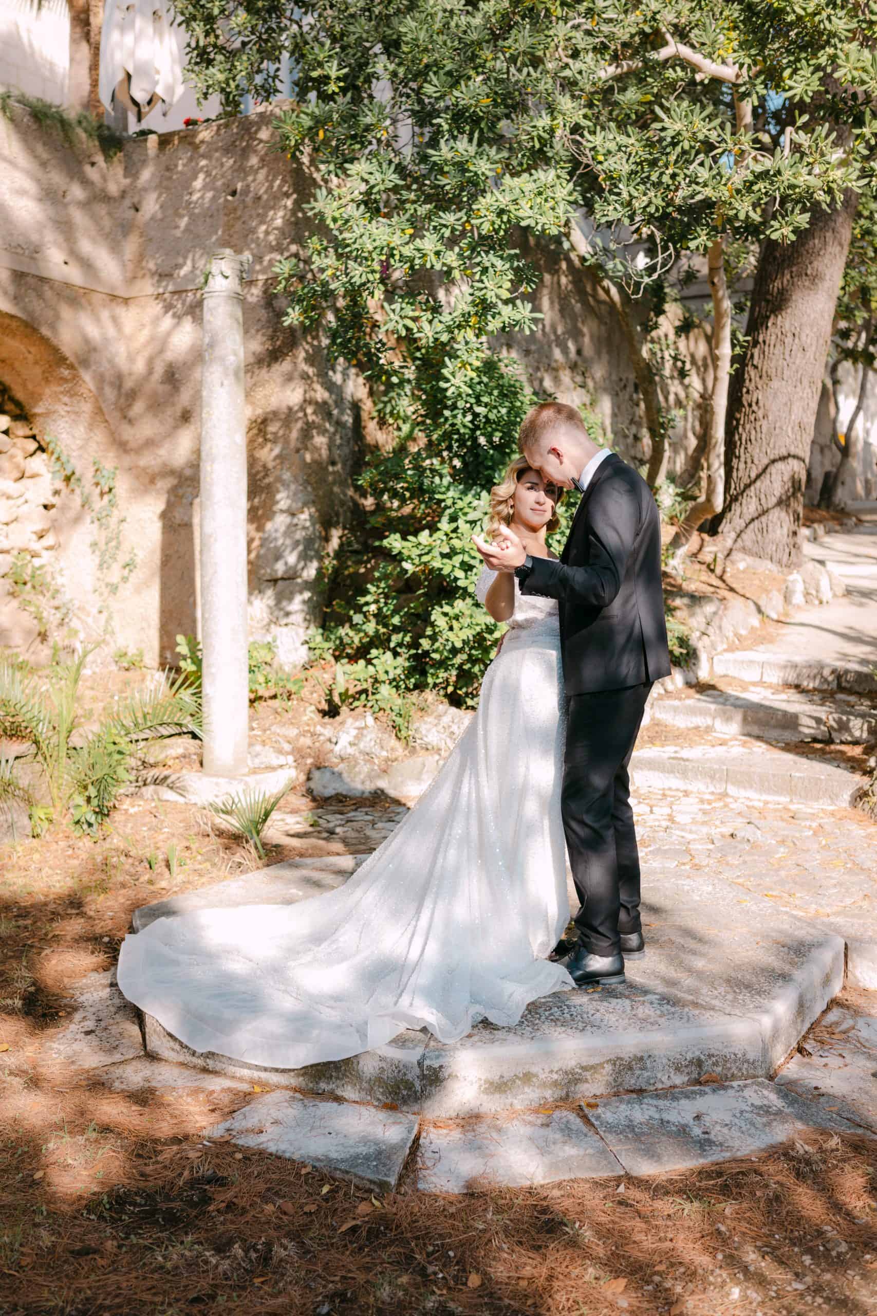 Mladenci plešu na malom kamenom podestu okruženi zelenilom i drvećem. Fotografija u boji iz wedding sessiona na otvorenom u Dubrovniku.