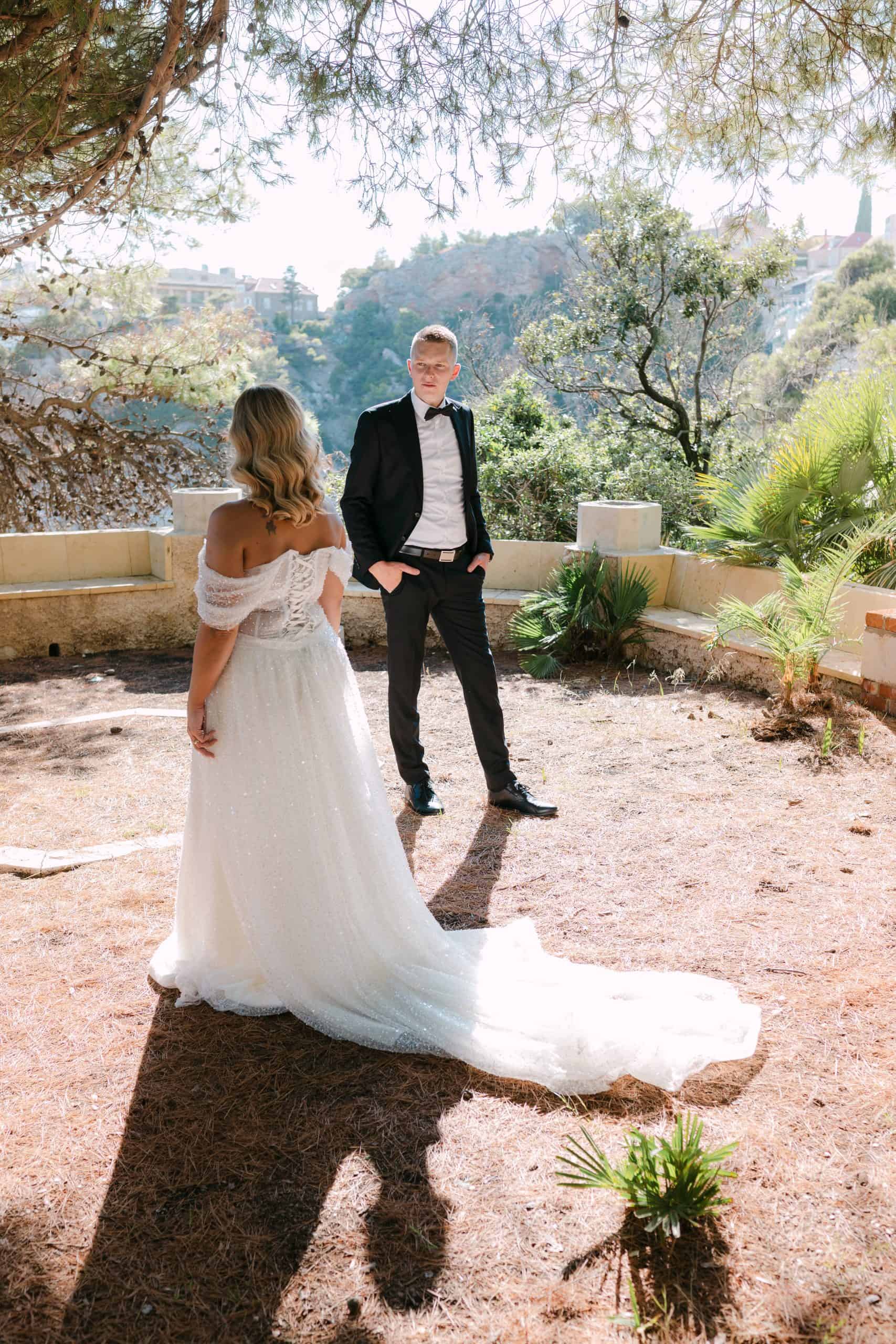 Mladenka okrenuta leđima kameri pokazuje dugački šlep vjenčanice, dok mladoženja gleda prema njoj. Stoje na vidikovcu s predivnim pogledom na more i obalu Dubrovnika.