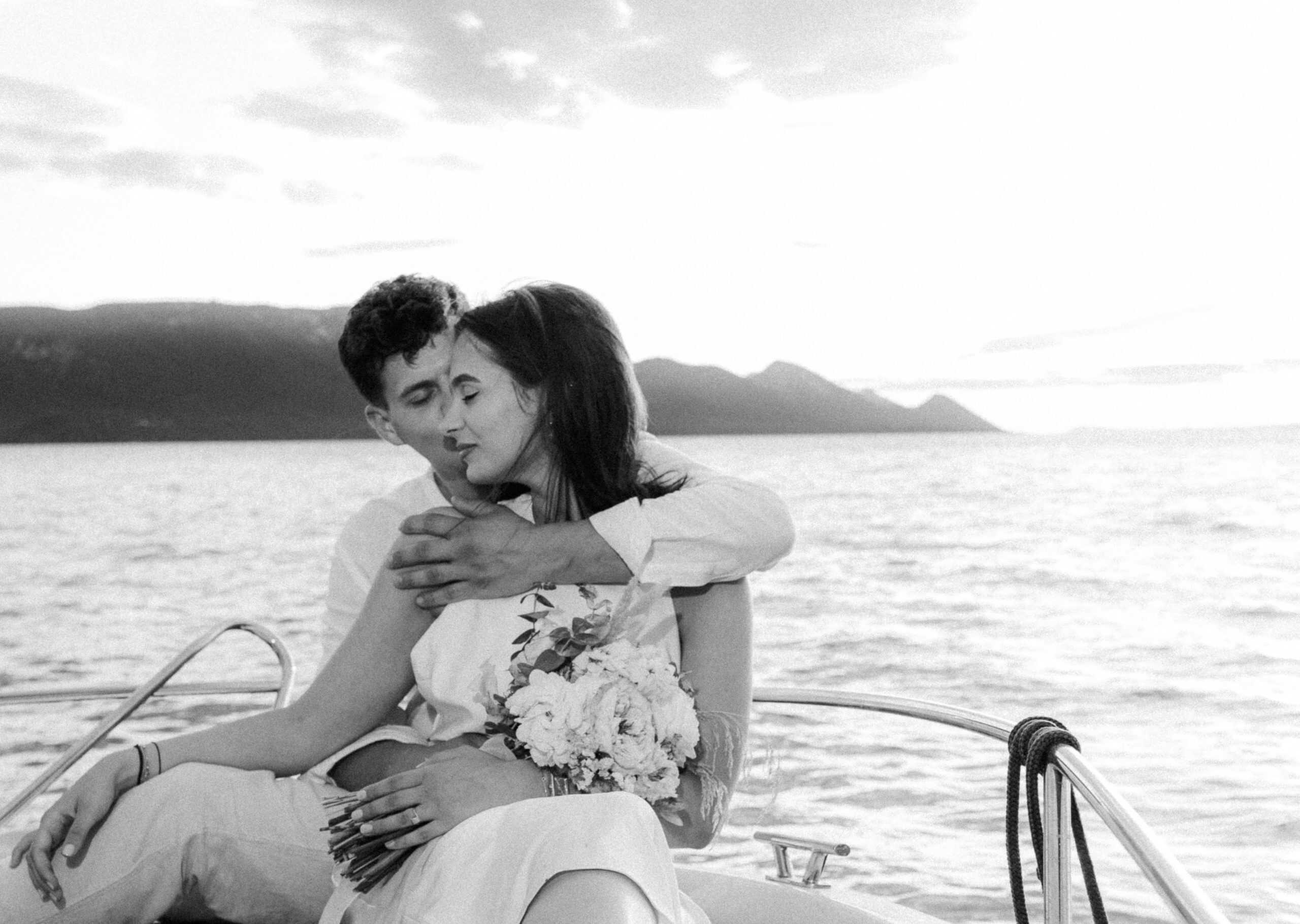 Filmski crno-bijeli kadar mladenaca koji uživaju u vožnji brodom. Mladoženja grli mladenku koja drži vjenčani buket, s planinama u pozadini.