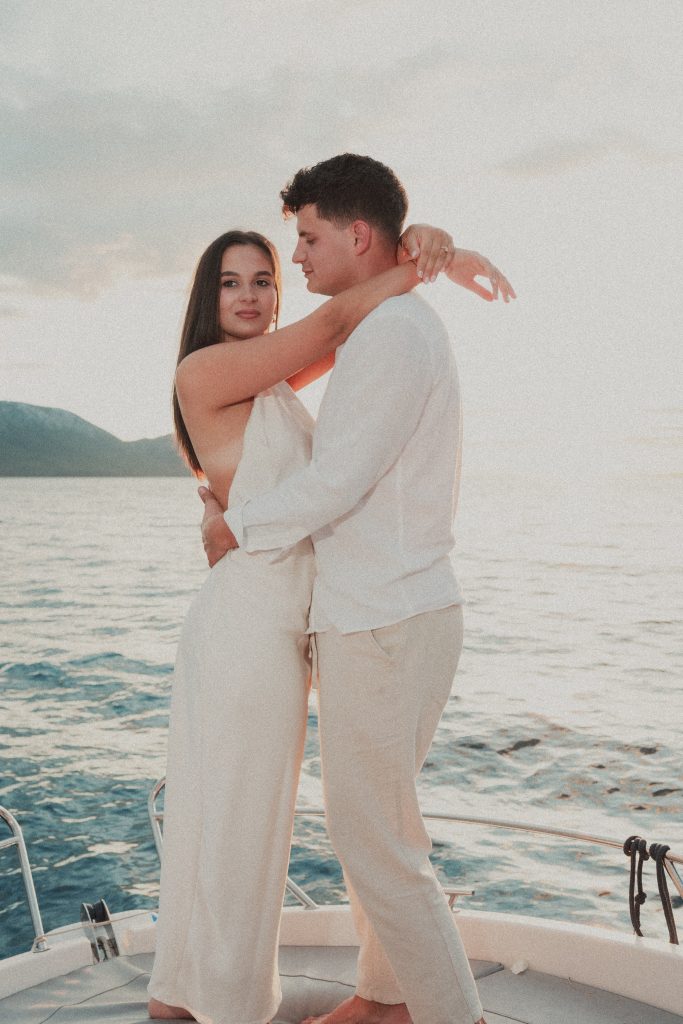 Romantični zagrljaj para na pramcu broda tijekom zalaska sunca. Editorial zaručnički session na moru uz tople, ljetne tonove.