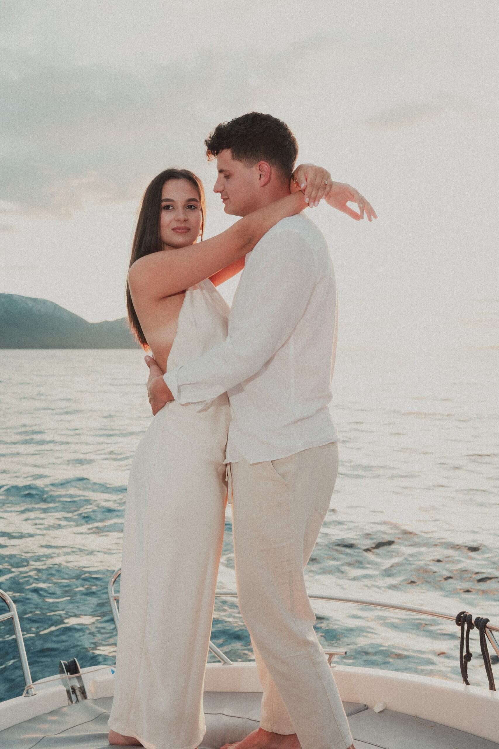 Romantični zagrljaj para na pramcu broda tijekom zalaska sunca. Editorial zaručnički session na moru uz tople, ljetne tonove.