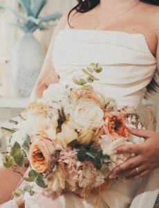 Krupni plan mladenke koja drži bogati vjenčani buket u pastelnim tonovima. Fokus na detalje vjenčanice, cvijeća i prstenja.