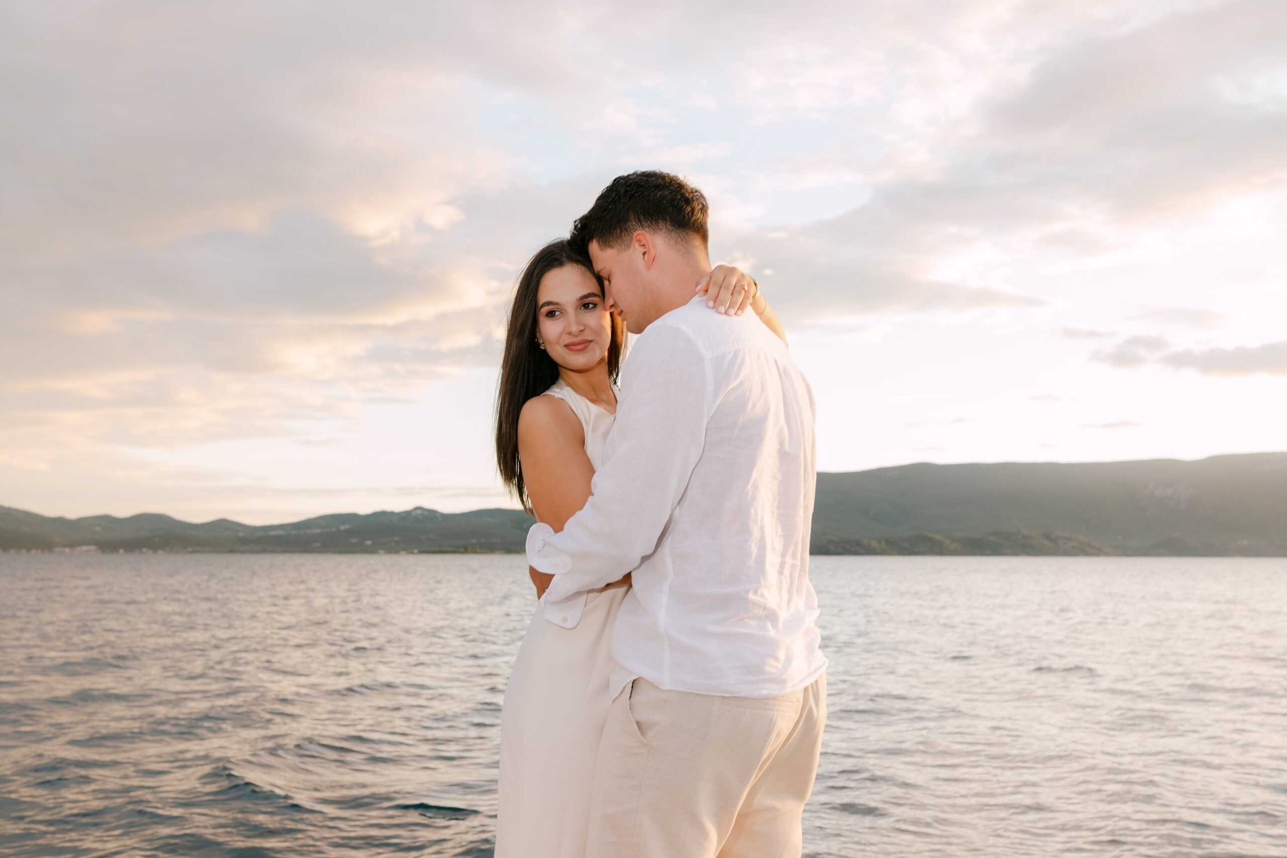 Budući mladenci u zagrljaju na brodu tijekom zalaska sunca na moru. Romantičan session zaruka s toplim ljetnim osvjetljenjem.